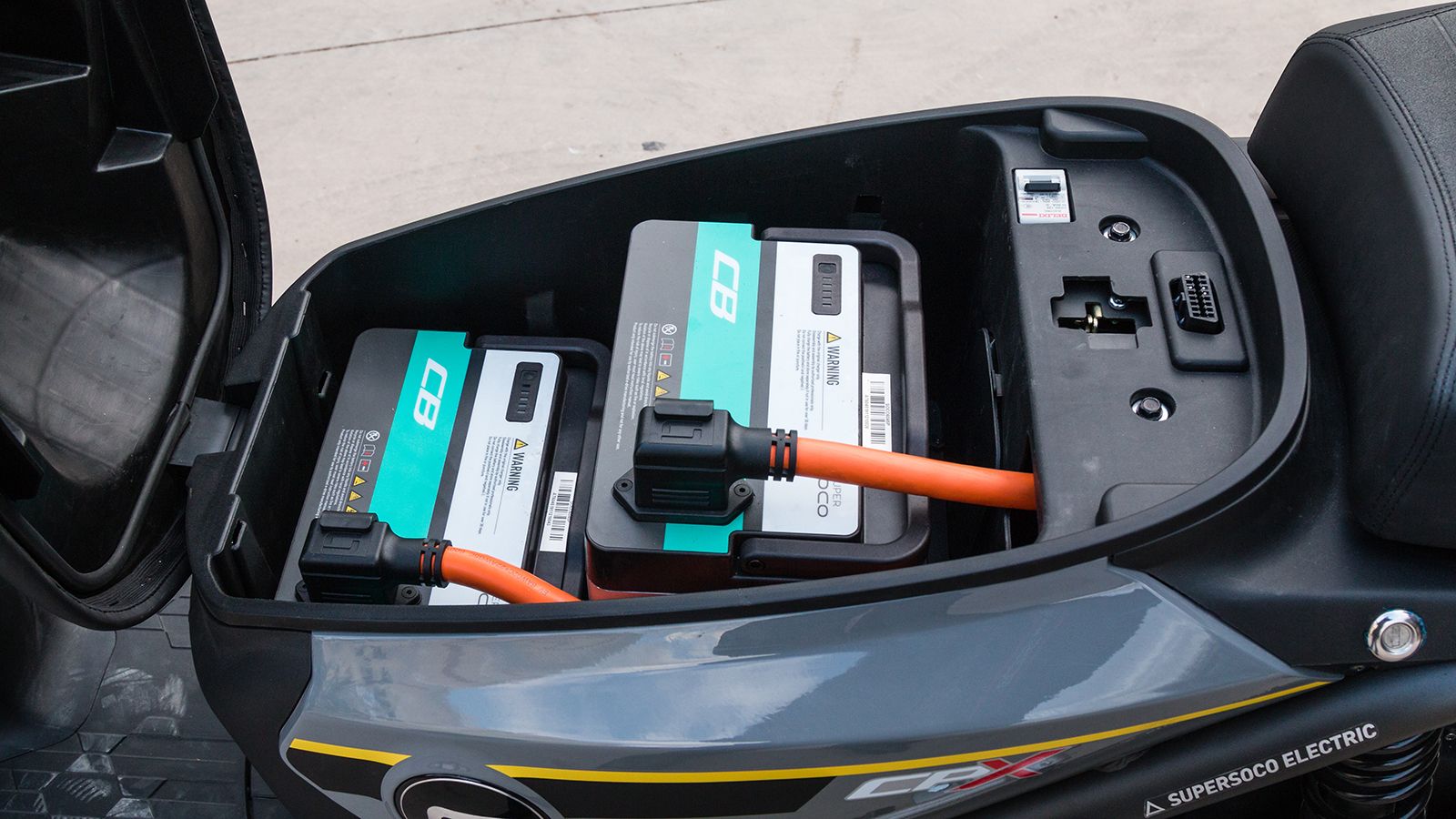 Κάτω από τη σέλα δεν υπάρχει ο παραδοσιακός χώρος για τοποθέτηση αντικειμένων. Αντί αυτού θα συναντήσουμε ένα φορητό φορτιστή, και κάτω από το πλαστικ