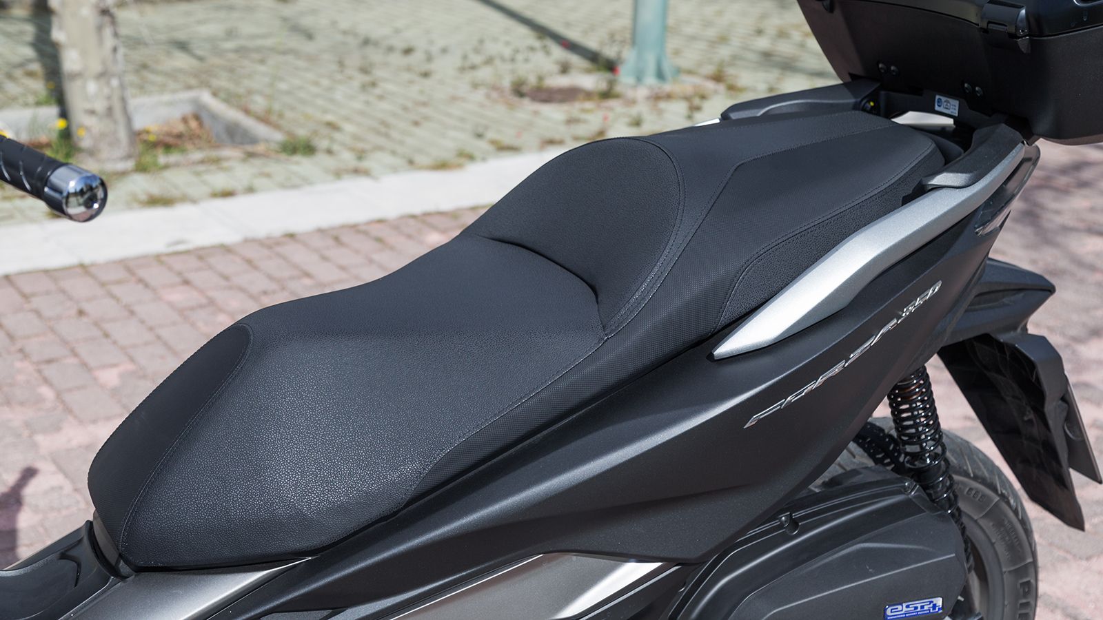 Η σέλα δύο επιπέδων διαθέτει μεγάλα τμήματα και φιλοξενεί με άνεση οδηγό και συνεπιβάτη. Ο πλαστικές χειρολαβές, αντί για αλουμινίου, επέφεραν μείωση 