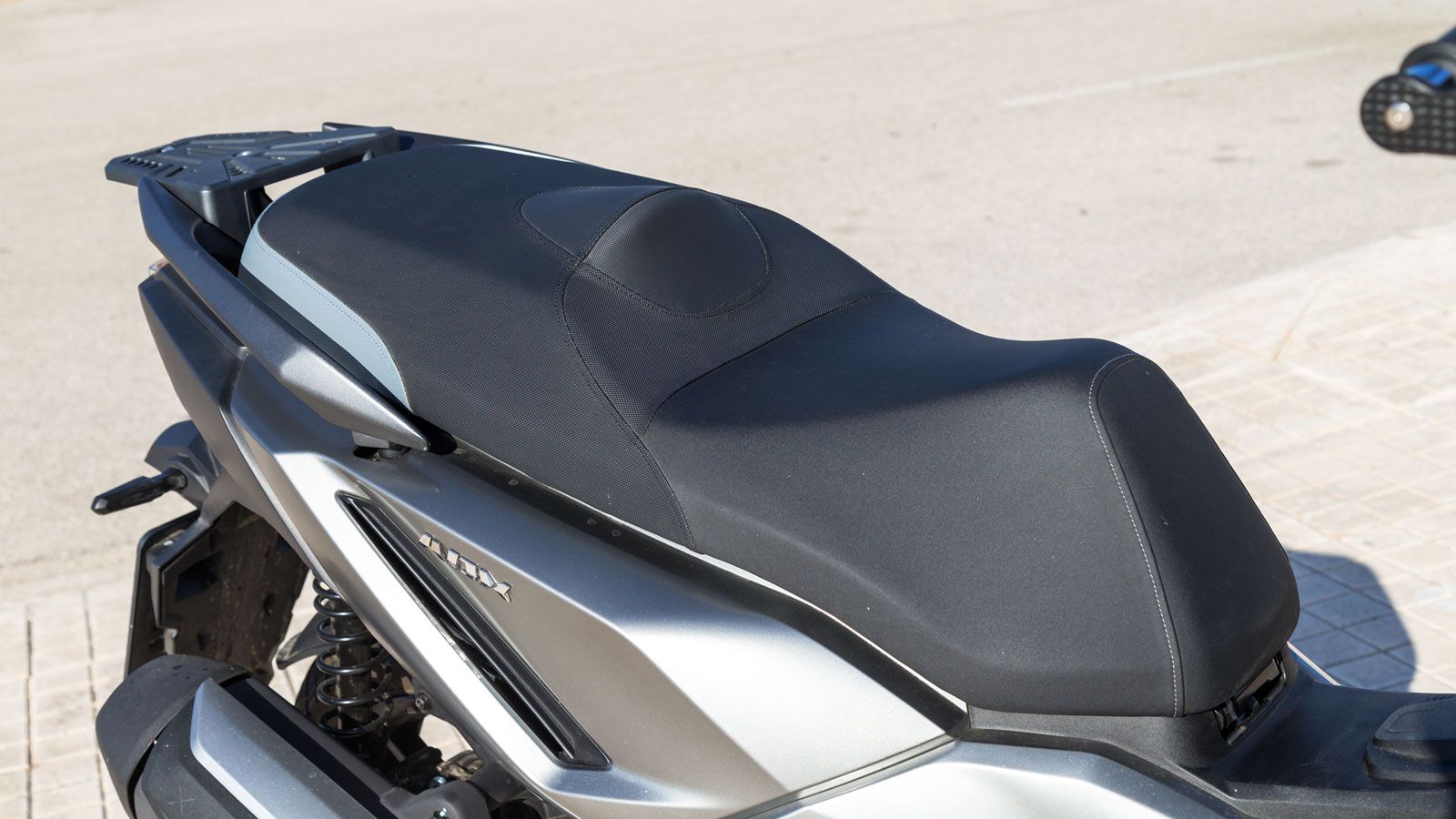 Παρά τον πιο «σκληροτράχηλο» σχεδιασμό του, το SYM ADX 300 παραμένει scooter στην ουσία του — δηλαδή άνετο και πρακτικό. Η σέλα βρίσκεται χαμηλά