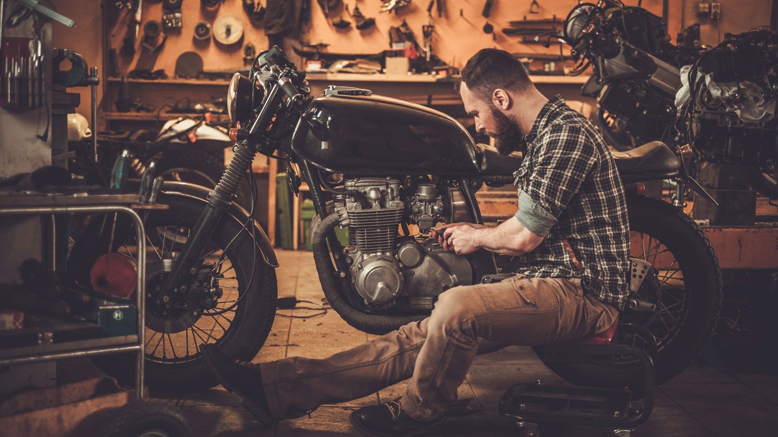Γκαράζ με μοτοσυκλέτα που την επισκευάζει ένας άντρας σε χαμηλό φωτισμό.