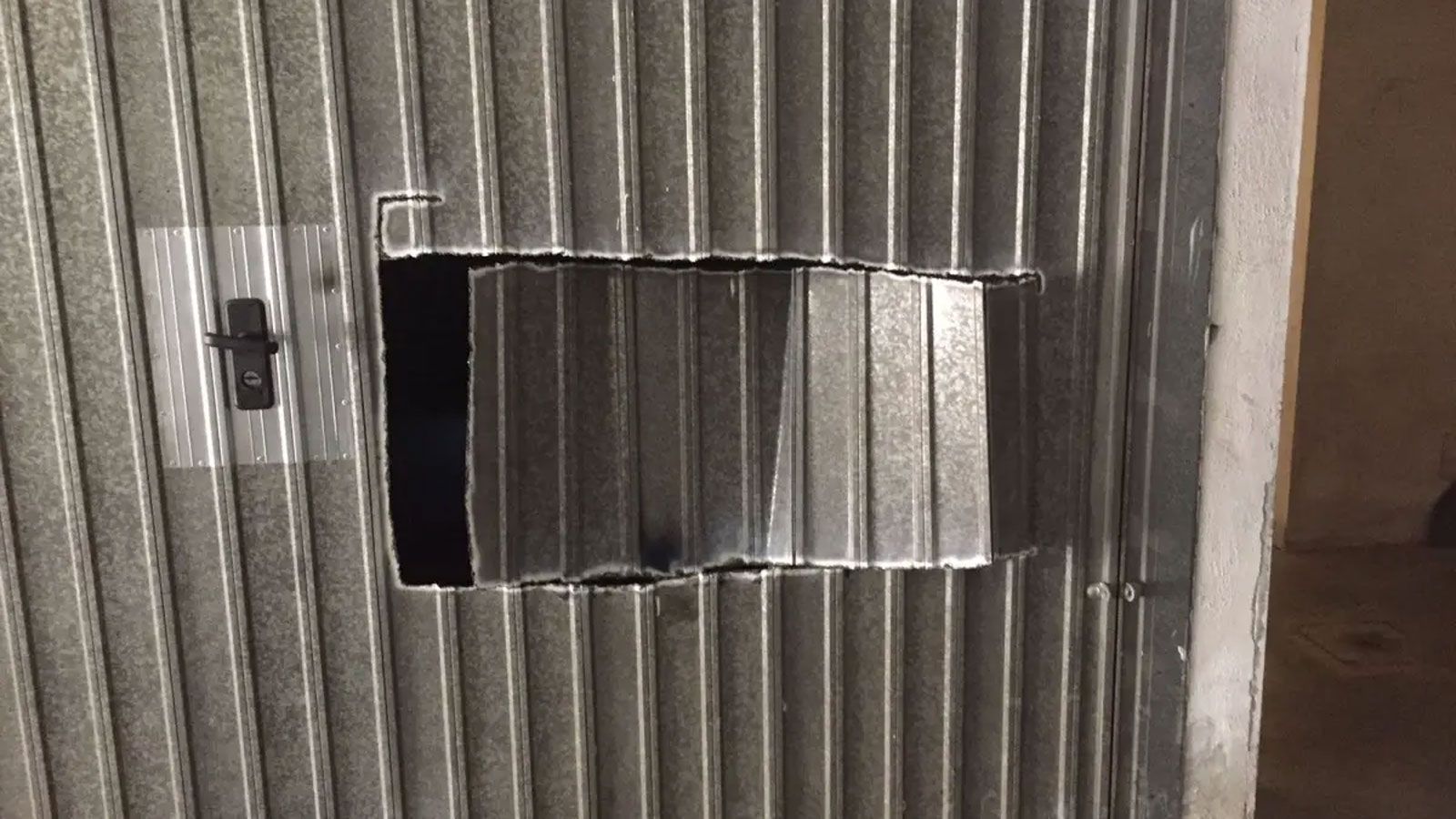 Μεταλλική πόρτα γκαράζ με μεγάλο κομμένο άνοιγμα, δείχνοντας πόσο εύκολα μπορεί να παραβιαστεί από κλέφτες μοτοσυκλετών.