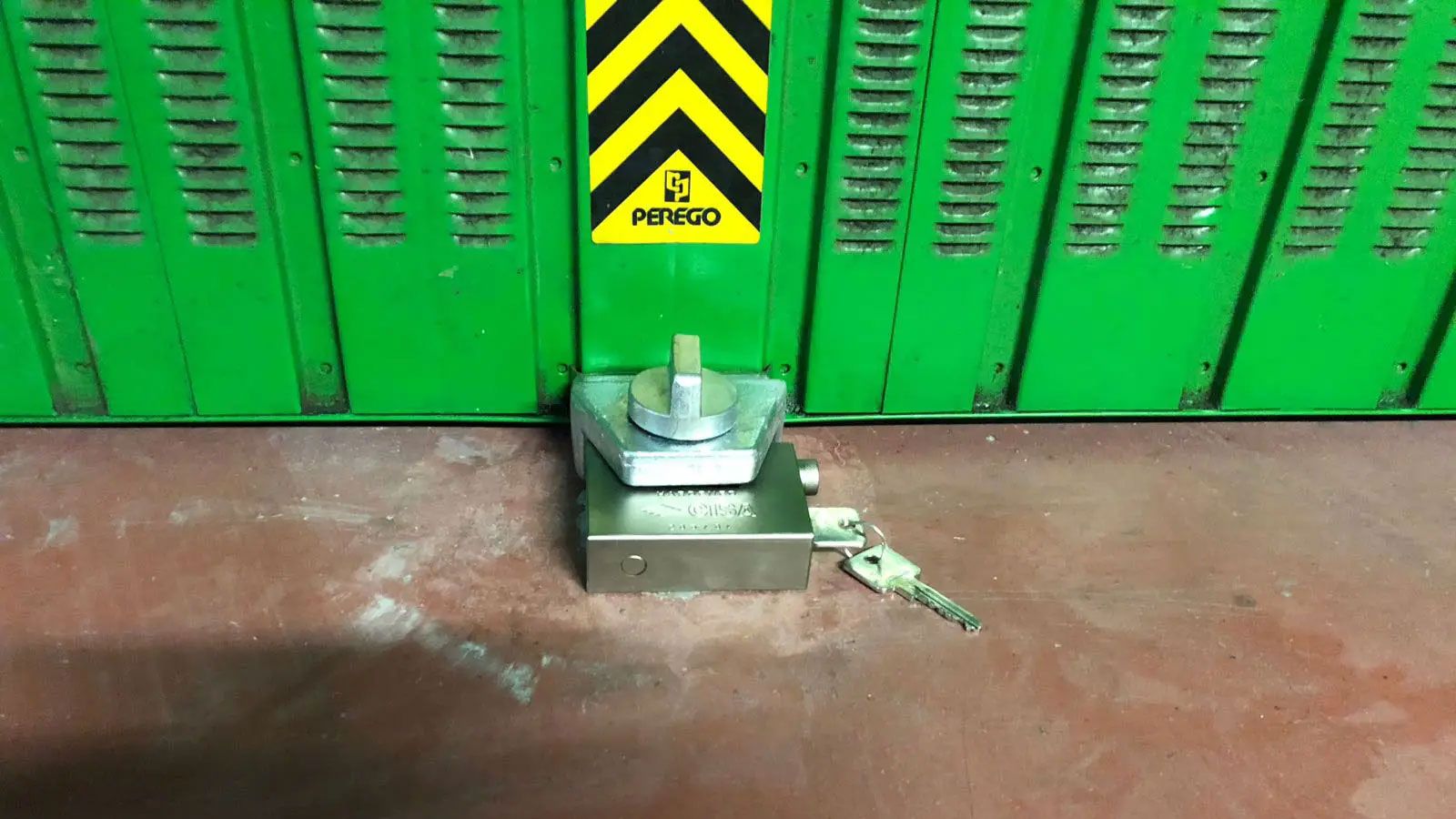 Μεταλλικός κρίκος αγκυρωμένος στο δάπεδο γκαράζ, σχεδιασμένος για να ασφαλίζει μοτοσυκλέτα με αλυσίδα.