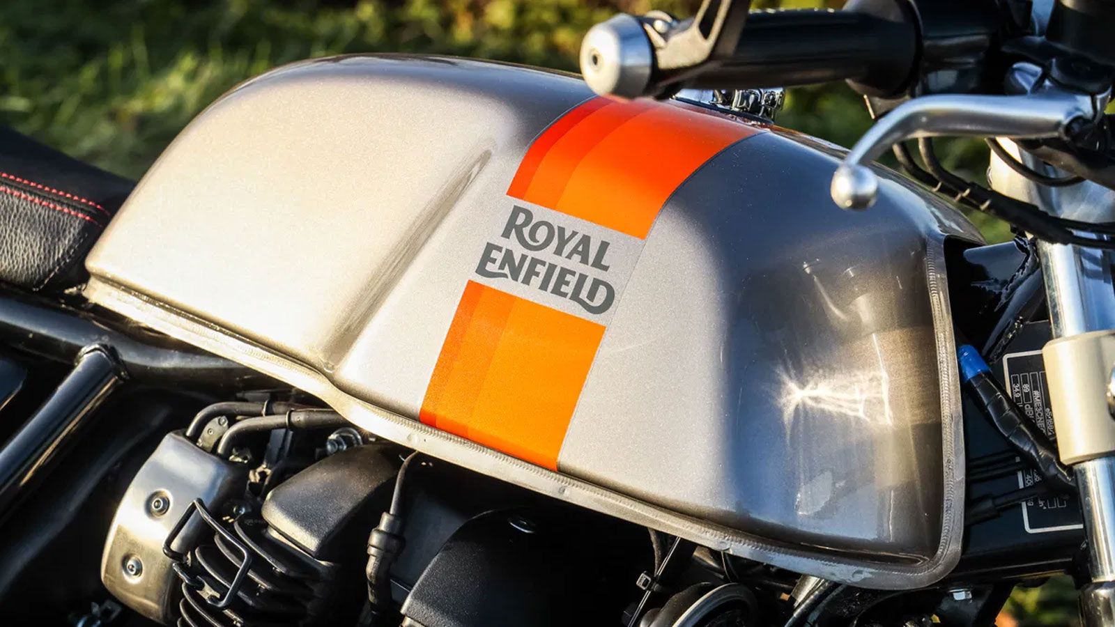 Λεπτομέρεια ρεζερβουάρ Royal Enfield με λογότυπο και πορτοκαλί ρίγα σε γκρι μεταλλικό φινίρισμα.