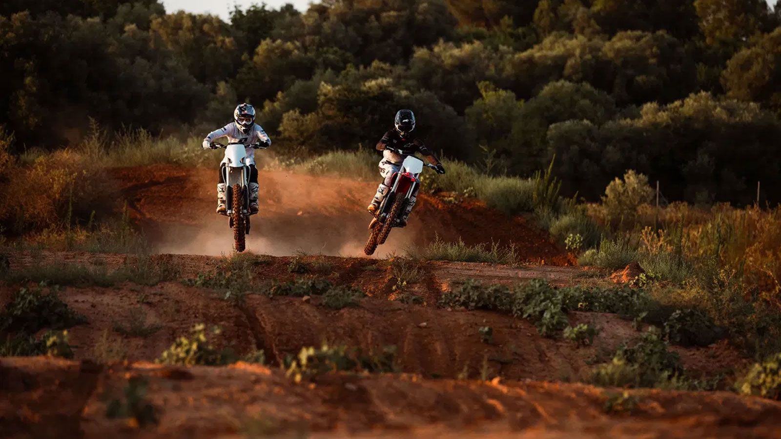 Δύο αναβάτες ηλεκτρικών motocross Stark Future σε άλμα σε χωμάτινη πίστα κατά τη δύση του ηλίου